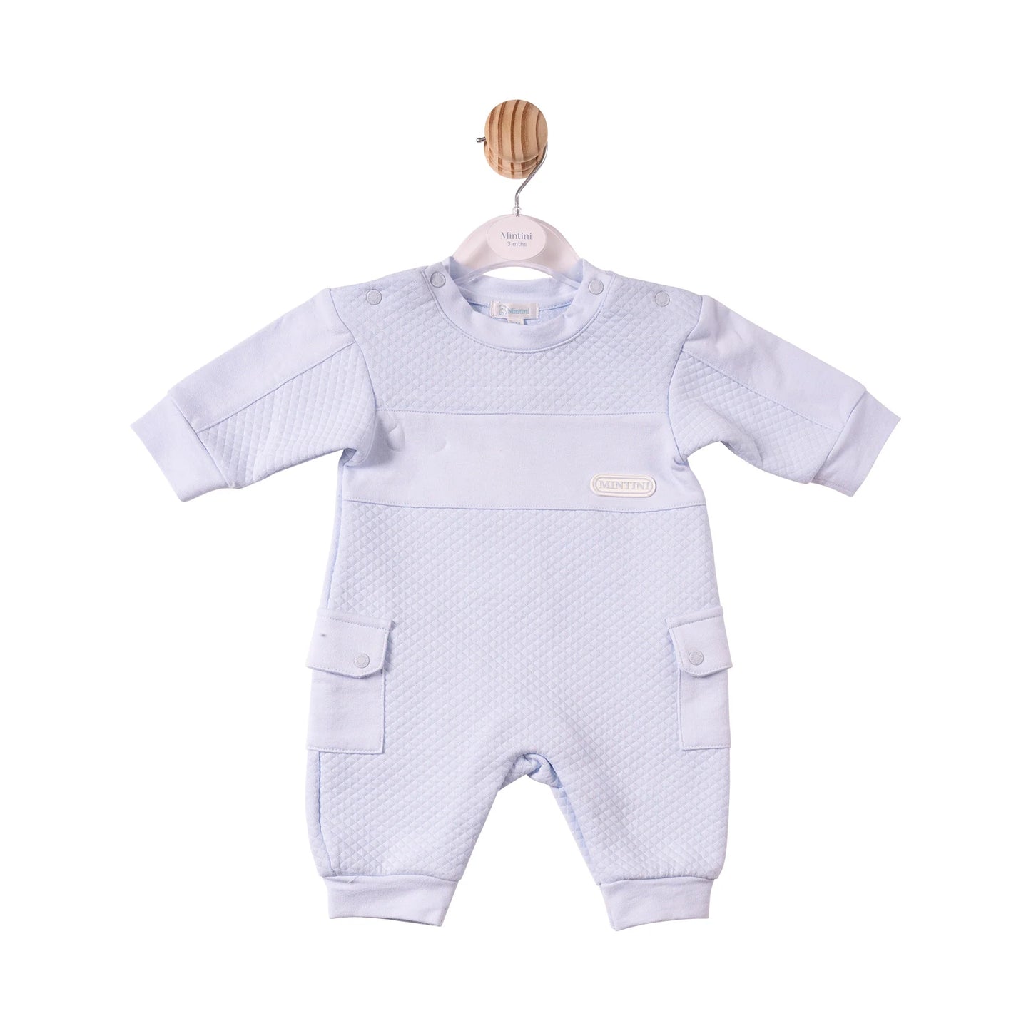 A baby's short-sleeve one-piece romper in a very pale lavender-blue colour, featuring a textured waffle-weave pattern across the chest and legs, side cargo pockets, and a small oval brand patch on the chest.