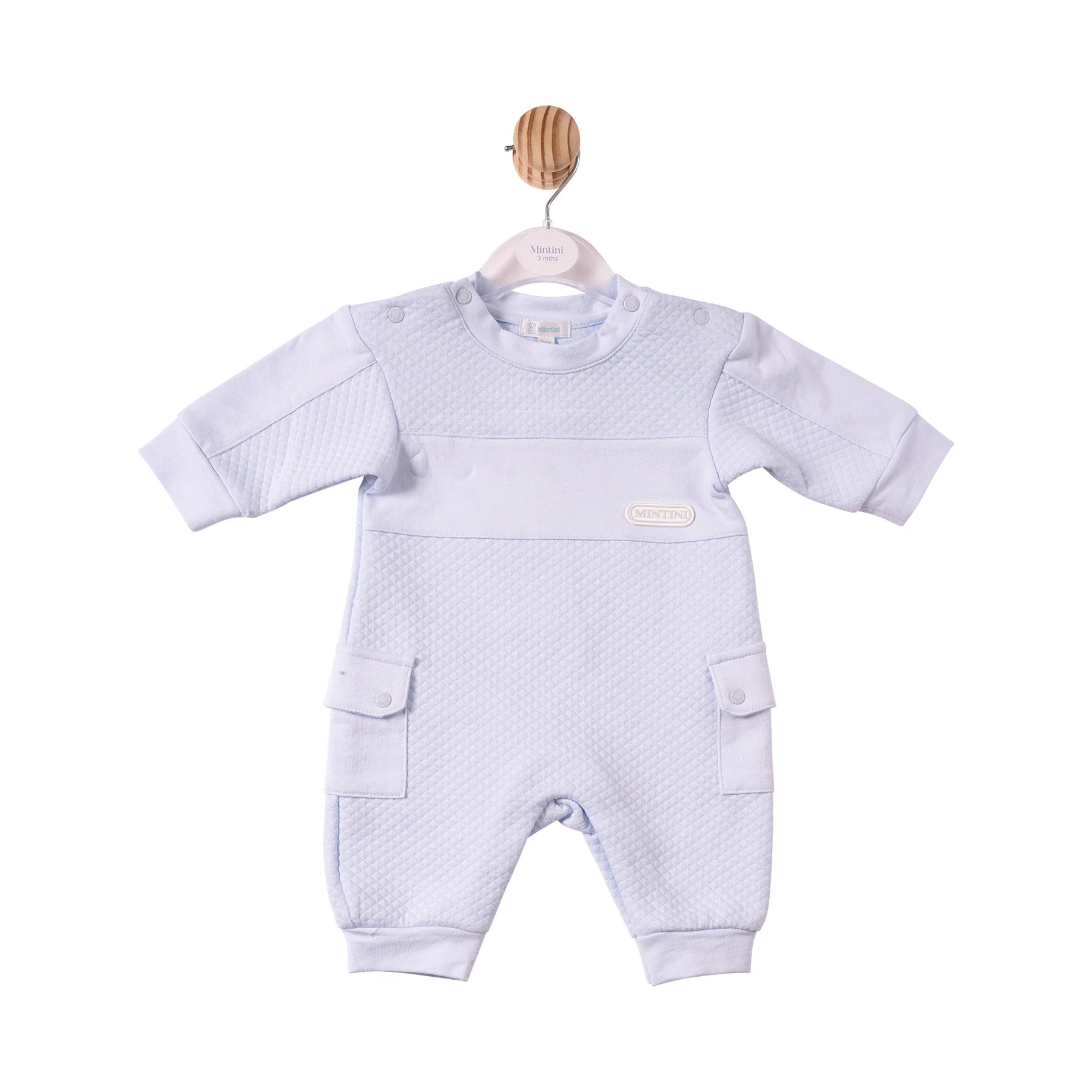 A baby's short-sleeve one-piece romper in a very pale lavender-blue colour, featuring a textured waffle-weave pattern across the chest and legs, side cargo pockets, and a small oval brand patch on the chest.