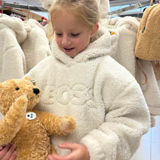 Child in a white fleece coat holding a teddy bear in a store setting